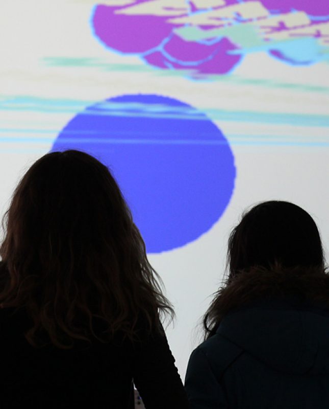 2 girls play a video game projected on a gallery wall